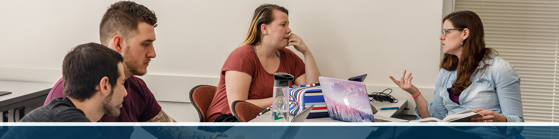 Four Forensic Psychology students discuss material at a table with their laptops.
