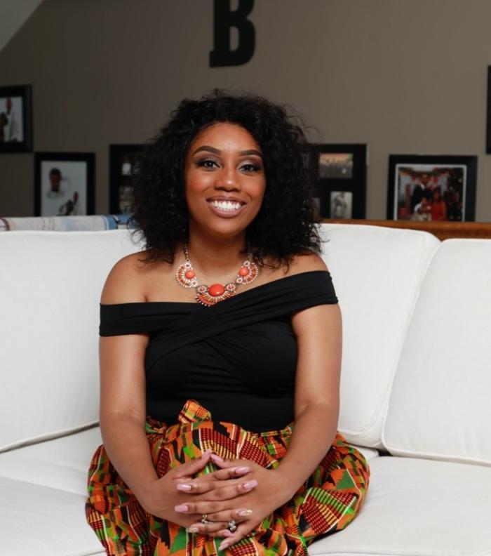 Image of a woman in a black top and colorful pants sitting on a couch.
