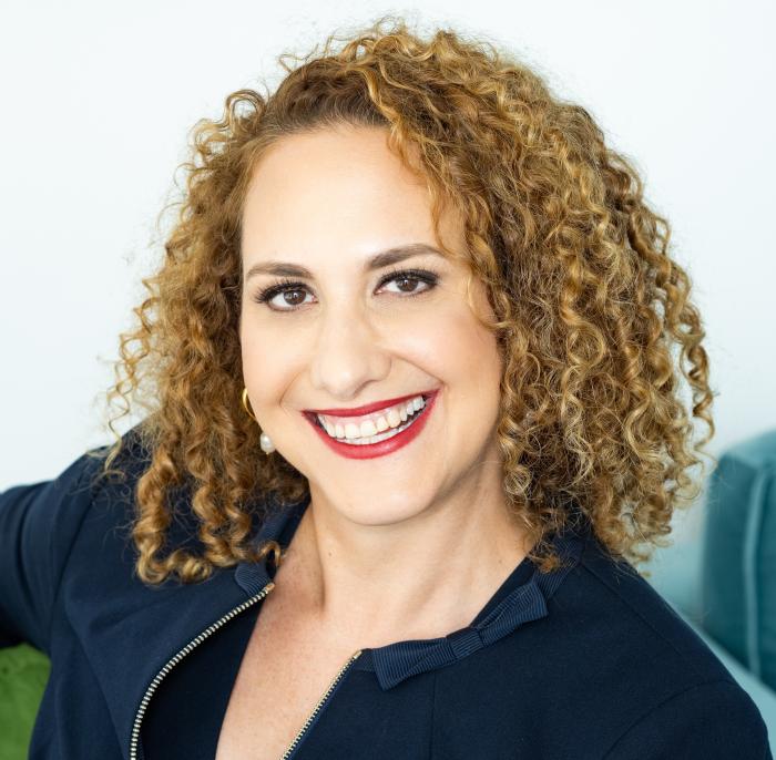 Image of a smiling woman with curly brown hair in a black shirt.